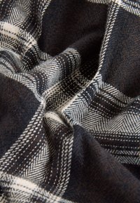 Uldblandet stof i mørk marineblå, hvid og brun ternet mønster. Har en blød, struktureret overflade med tydelige sildebens- og ternedesign.