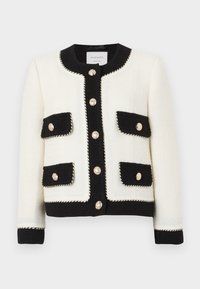 Veste en tweed noir et blanc avec col rond, poches avant et boutons ornés. Présente un bord en tresses le long des bords.