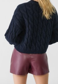 Maglione a costine di colore blu navy con collo alto e maniche a palloncino, abbinato a pantaloni corti in pelle bordeaux. Tessuto morbido e vestibilità rilassata.