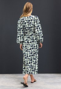 Robe longue en tissu à motifs avec des dessins géométriques bleu et crème. Manches bouffantes et taille cintrée mettent en valeur la silhouette.