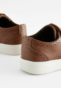 Baskets en cuir marron avec des accents perforés, semelles en caoutchouc texturé blanc et talons arrondis. Présentent une finition lisse et un design basse.