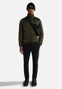 Giacca imbottita verde oliva, pantaloni neri, scarpe nere, borsa a tracolla nera, berretto nero, occhiali da sole, vista frontale, accessori minimali.