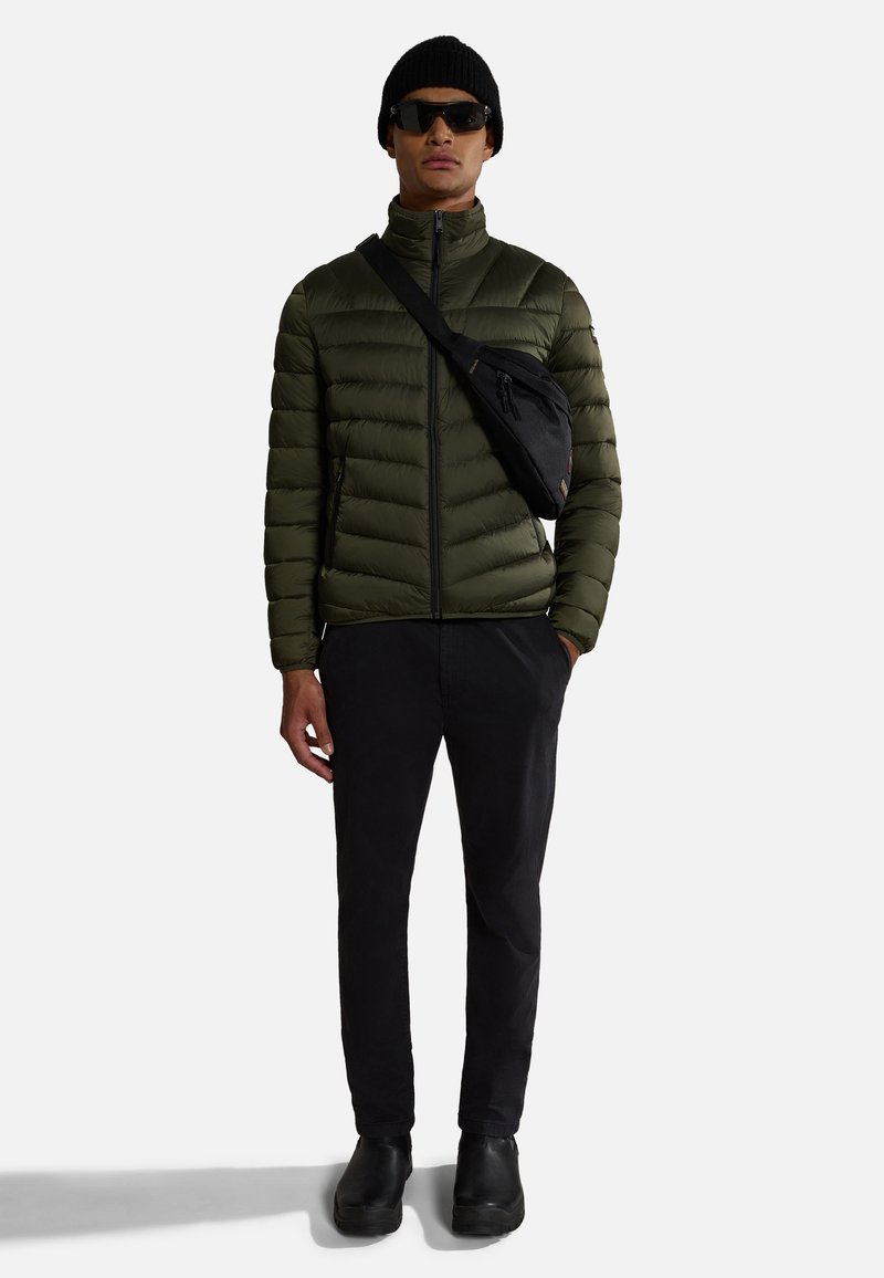 Oliwkowa, ocieplana kurtka, czarne spodnie, czarne buty, czarna torba na ramię, czarna czapka beanie, okulary przeciwsłoneczne, widok z przodu, minimalna biżuteria.