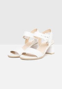 White sandals with a glossy finish, open toe, and wide straps. Features an adjustable ankle strap and chunky heel for support.