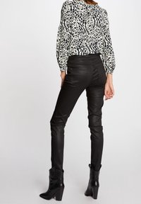 Czarne dopasowane spodnie o połyskującej fakturze, w połączeniu z bluzką w biało-czarny wzór w panterkę. Modelka ma na sobie czarne botki na obcasie.