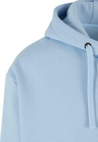 Svijetloplava dukserica s kapuljačom koja ima vezicu na izrezima i mekani, teksturirani materijal. Dizajn uključuje ležeran kroj i rebraste detalje.