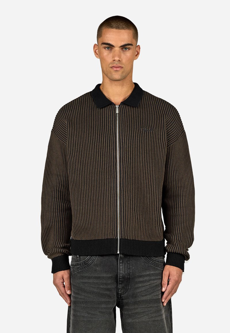 Rjava rebrasta jakna z zipom in črnim ovratnikom ter manšetami, ki se ponaša z drzno vertikalno črtasto zasnovo in zapiranjem na zadrgo. Teksture tkanine in minimalno blagovno znamko.