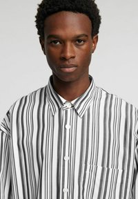 Koszula na guziki wykonana z bawełny z pionowymi czarno-białymi paskami, z kołnierzem, kieszenią i klasycznym zapięciem na guziki.