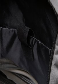 Unutrašnjost sive platnene torbe s crnim oblogom; sadrži strukturalnu površinu i platnenu petlju za pričvršćivanje predmeta. Vidljivo zatvaranje na munju.