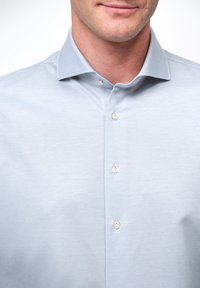 Camisa de botones azul claro con patrón de espiga, cuello puntiagudo y botones blancos, confeccionada en un tejido suave.