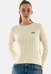 Jersey de punto trenzado color crema con cuello redondo y puños acanalados. Presenta un logo bordado en el lado izquierdo del pecho.