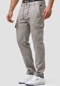 Jasnoszare spodnie cargo z przednimi kieszeniami, bocznymi kieszeniami cargo i zapięciem na guzik. Połączone z białymi sneakerami i czarnym pasem.