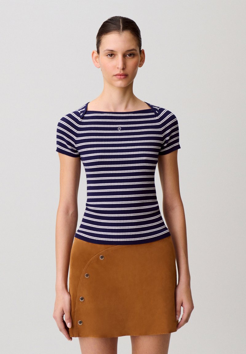 Top a righe navy e bianco con collo quadrato e maniche corte, abbinato a una minigonna marrone in suede con dettagli circolari in metallo.