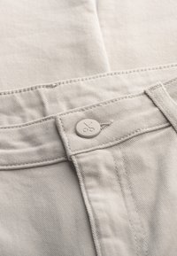 Lichtgrijze katoenen broek met een gladde textuur, voorzien van een eenvoudige tailleband en een knop met een schaarontwerp voor sluiting.