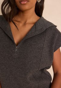 Gray knitted sleeveless top featuring a zip closure, wide collar, and soft texture, highlighting a relaxed fit and minimalist design.