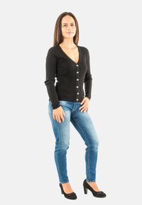 Cardigan nero a coste con bottoni, abbinato a jeans azzurri alla caviglia e scarpe con tacco nere. Design semplice e aderente.