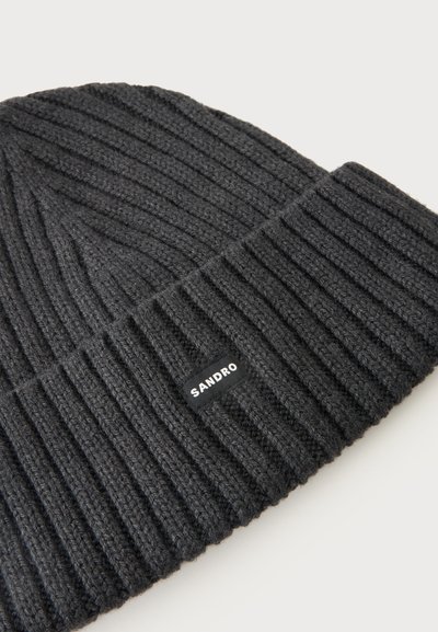 Bonnet en maille côtelée gris foncé avec revers plié et petite étiquette "SANDRO" sur le revers, présenté sur un fond clair.
