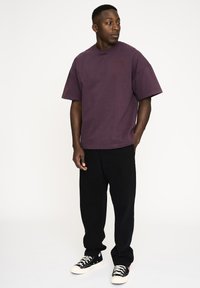 Lilla oversized t-shirt med korte ærmer, prydet med et diskret logo på brystet. Bæres med løse sorte bukser og sorte sneakers.