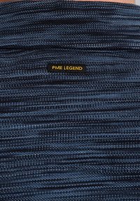 Tmavo modrá pletená látka s horizontálnymi pruhmi a textúrovaným povrchom. Obsahuje čiernu nášivku s nápisom "PME LEGEND" v žltom písmene.