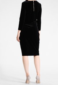 Svart sammetklänning med långa ärmar, figursydd silhuett, rynkdetalj vid midjan och gulddragkedja bak. Bärs med ljusgrå klackar.