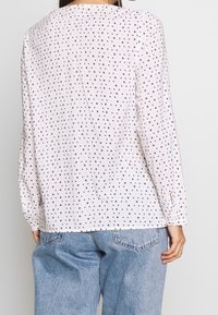 Blusa rosa chiaro con pois neri e dorati, maniche lunghe e vestibilità comoda. Presenta un collo rotondo e un dettaglio di plissettatura sul retro.