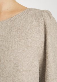 Maglione beige a maglia con scollatura rotonda, tessuto testurizzato e maniche a sbuffo. Il materiale appare morbido e ha una leggera lucentezza.