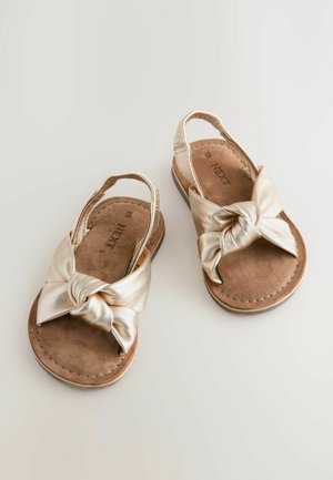 Guldmetalliske sandaler med en knyttet sløjfedesign, overdel i kunstlæder og indersål i brunt ruskind. Slingback-stil med flade såler.