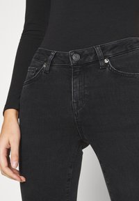 Jeans de mezclilla negra de cintura alta, con cierre de botón, bolsillos frontales y una textura suave. Vista en primer plano que resalta los detalles.