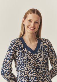 Navy-Bluse mit beigem Blattmuster, V-Ausschnitt, langen Ärmeln und gerafftem Bund. Hergestellt aus glattem Stoff mit lockerer Passform.