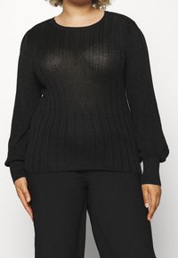 Zwarte geribbelde gebreide trui met lange pofmouwen en een ronde halslijn. Heeft een subtiele glans en een textuurpatroon doorheen.