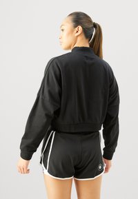 Sweatshirt noir coupe courte avec col rond, poignets côtelés et coupe décontractée, associé à un short de sport noir avec des accents blancs.