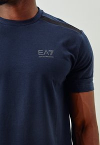 Navy blue short-sleeve t-shirt, made of smooth fabric, featuring a subtle logo and textured shoulder accents.