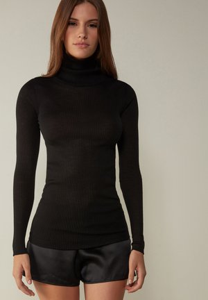 Svart ribbad polotröja med långa ärmar. Texturerad tyg och åtsittande design. Kombinerad med glänsande svarta satinshorts under midjan.