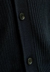 Cardigan tricoté marine avec une texture en côtes et une fermeture par bouton noir. Le tissu est doux avec des détails de couture en tricot visibles.