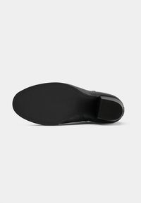 Semelle de chaussure en cuir noir avec un design lisse et plat, bout arrondi et un léger talon. La surface est texturée avec une finition propre et minimaliste.