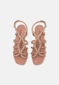 Blush rosa sandaler med kryssende stropper, utsmykket med gullbeslag og rhinesteiner, med en myk semsket tekstur og justerbare ankelstropper.