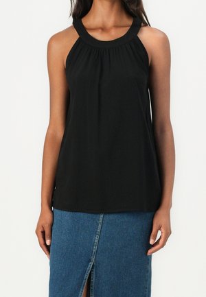 Kobieta ubrana w czarny, bezrękawnikowy top na szyję, zestawiony z niebieską denimową spódnicą z przednim rozcięciem.