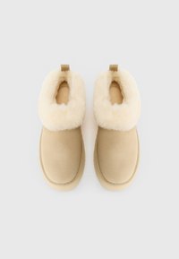 Zapatillas de invierno de color beige, sin cordones, con un grueso forro de felpa color crema alrededor de la abertura, mostradas desde arriba sobre un fondo blanco.