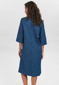 Vestido de denim con mangas tres cuartos, corte relajado, largo medio y detalles de costura visibles. Tejido azul con una textura suave.