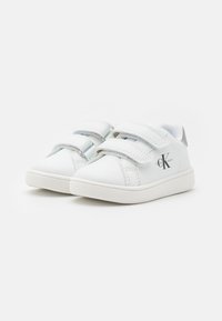 Witte kindersneakers met klittenbandsluitingen, gemaakt van glad synthetisch materiaal, met een ronde neus en subtiele logo-accenten aan de zijkant.
