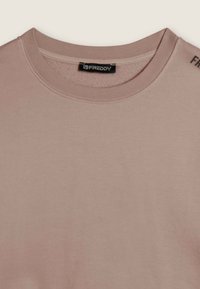 Camiseta de algodón rosa empolvado con escote redondo, mangas cortas y una etiqueta negra con el logo "FREDDY" en el cuello. Textura suave y lisa.
