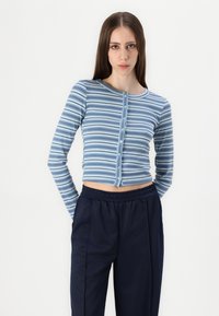 Top cropped de mangas compridas listrado em azul e branco, com decote redondo e fecho frontal de botões, combinado com calças de cintura elástica azul-marinho.