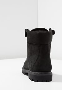 Black suede ankle boot with a textured finish, rounded toe, and a rugged rubber sole. Features a pull tab for easy wear.