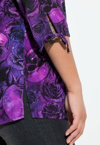 Paarse shirt met korte mouwen, voorzien van een bloemen- en schedelpatter, met een gestructureerde stof en strikdetails op de mouwen.
