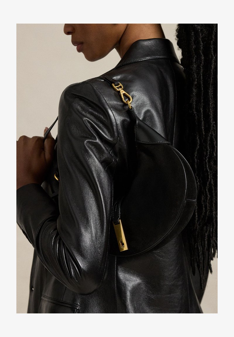 Asmuo dėvi juodą odinę striukę ir juodą pusmėnulio formos rankinę su auksinės spalvos detalėmis ant peties.