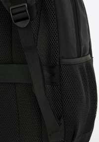 Sac à dos noir avec des détails en maille sur les côtés, des bretelles ajustables et un tissu lisse avec une fermeture éclair pour un rangement sécurisé.