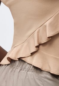 Κοντινή λήψη του μπεζ ριγέ άνω μέρους συνδυασμένου με ανοιχτό γκρι ελαστικό παντελόνι μέσης σε ένα άτομο.