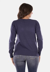 Maglione a maglia blu navy con maniche lunghe, orlo a coste e texture liscia. Indossato con jeans in denim chiaro, mostrando la vista posteriore e la vestibilità naturale.