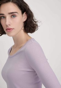 Lange mouw top in licht lavendel, gemaakt van gladde stof. Heeft een ronde halslijn en een getailleerd ontwerp. Minimalistische stikselaccenten.