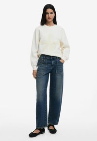 White sweatshirt with textured floral design; casual blue wide-leg jeans; black slip-on shoes. Relaxed fit with visible stitching details.